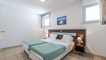 A hotel room with a double bed, two bedside tables with lamps, a window with curtains, and a painting on the wall.
