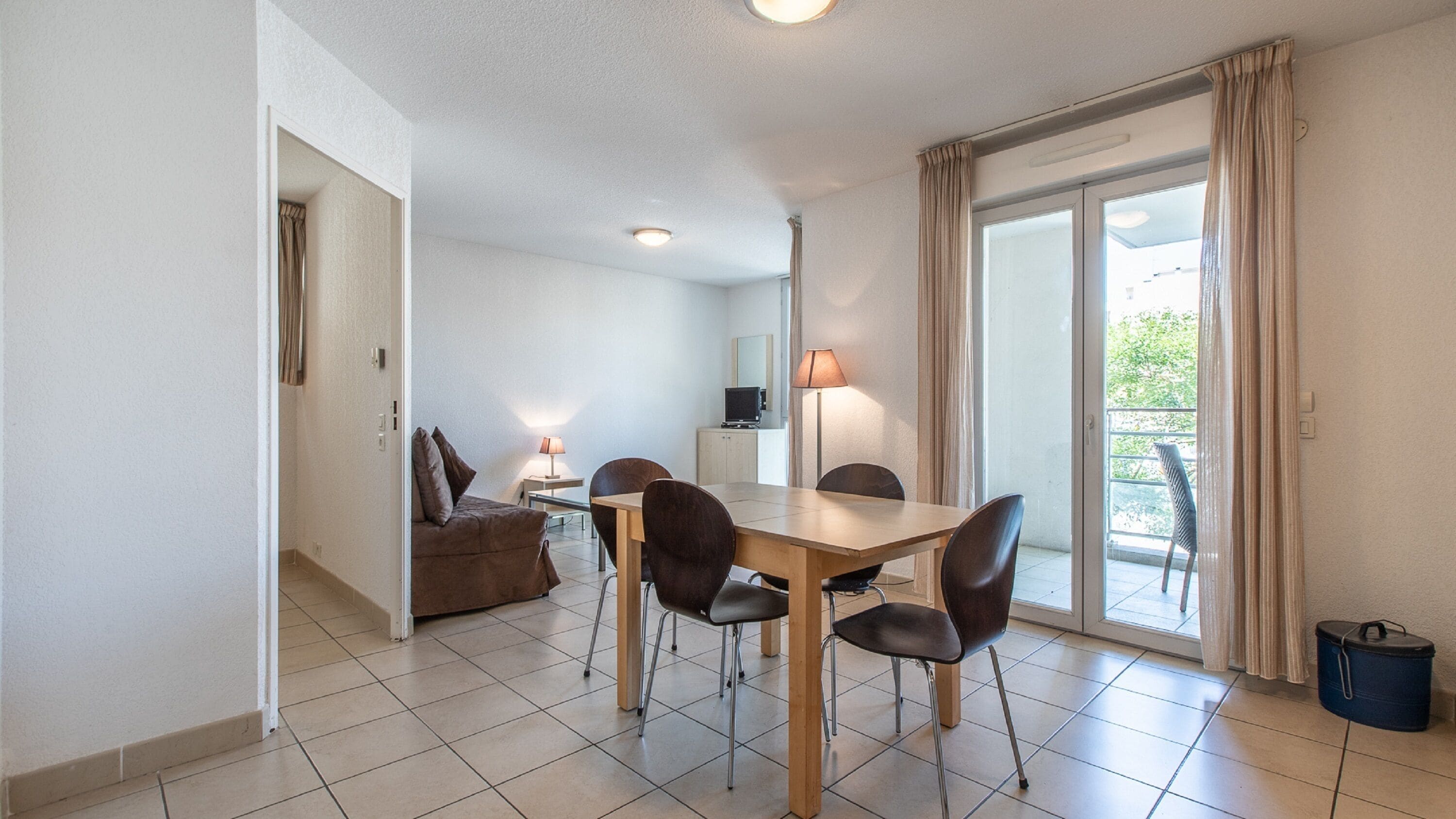 A dining area with a table and chairs, a sofa, a lamp, and a television.