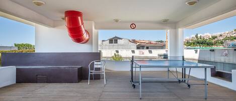 Eine Dachterrasse mit Tischtennisplatte, einer Sitzecke und einem roten Feuerwehrschlauch.