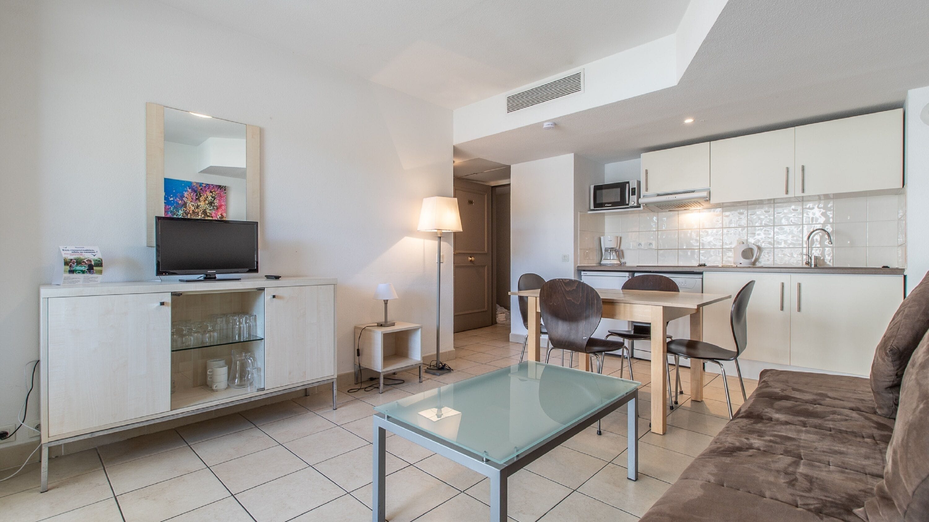 Um espaço compacto com cozinha compacta, área de jantar com mesa de vidro, sofá e televisão em um móvel.