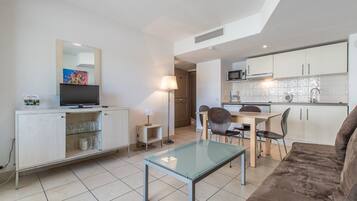 Um espaço compacto com cozinha compacta, área de jantar com mesa de vidro, sofá e televisão em um móvel.