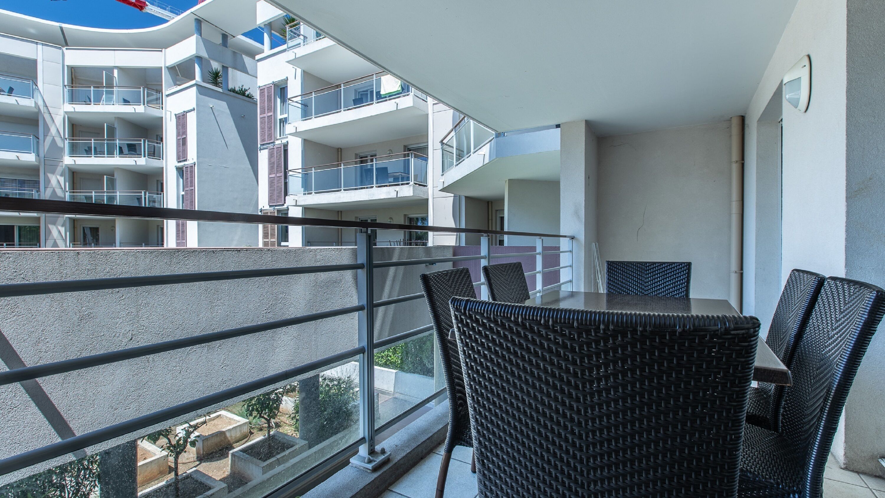 A balcony with wicker chairs and a table, overlooking a modern building with multiple balconies.