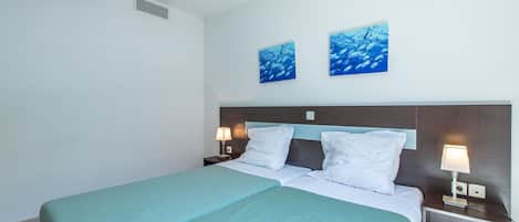 A hotel room with a bed, two nightstands, a wall-mounted vent, and two framed artworks above the bed.