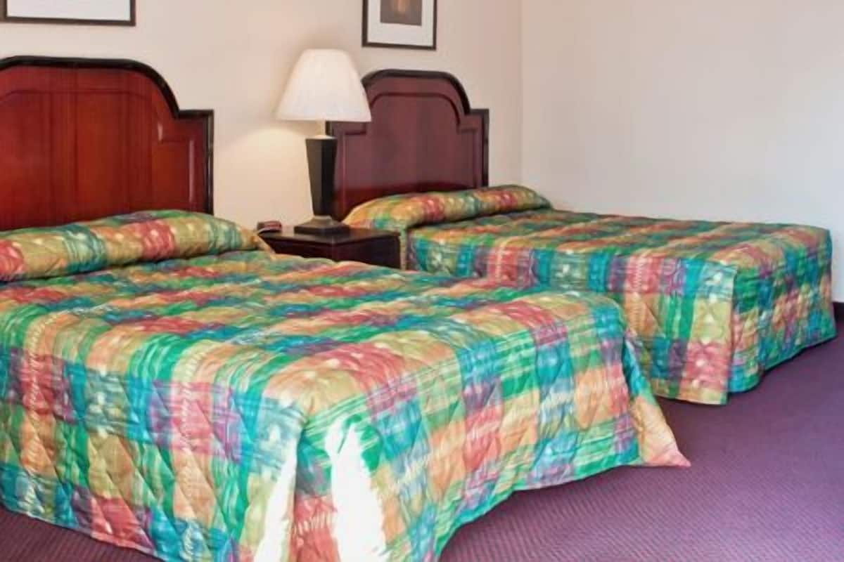 A hotel room with two beds, each with a colorful quilted bedspread. There are framed pictures on the wall, a bedside table with a lamp, and a wooden headboard.