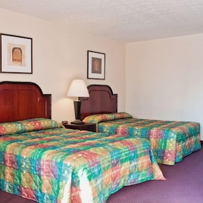 Habitación de hotel con dos camas, cada una con una colcha acolchada de colores. Hay cuadros en la pared, una mesita de noche con una lámpara y un cabecero de madera.