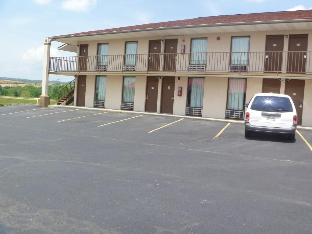 A motel with a two-story structure, a parking lot, and a white car parked in the lot.
