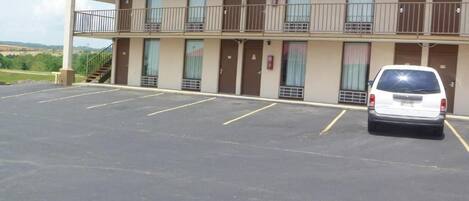 A motel with a two-story structure, a parking lot, and a white car parked in the lot.