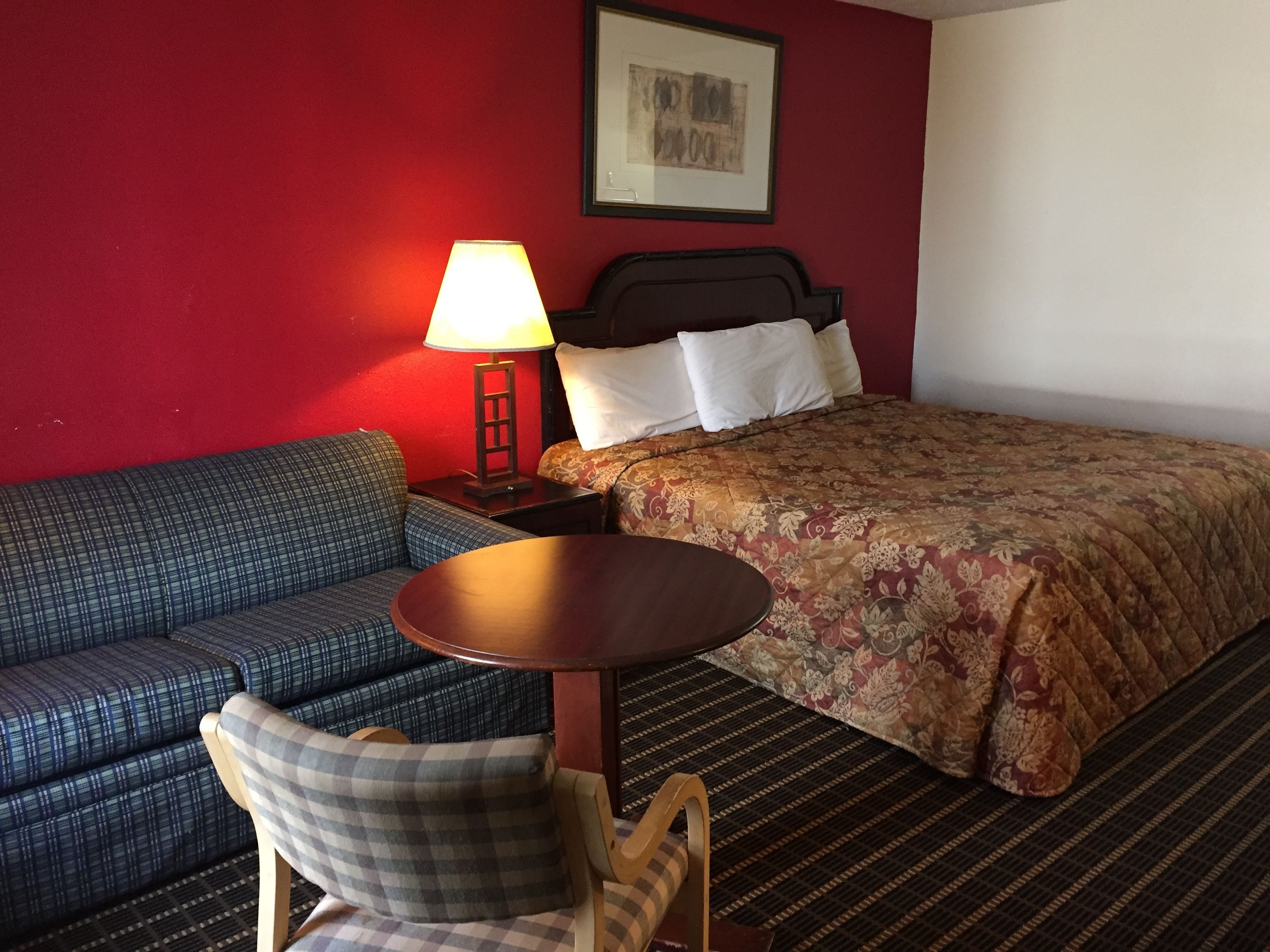Una habitación de hotel con cama, sofá, sillón, una mesita y una lámpara.