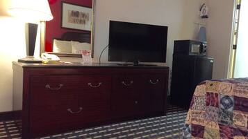 A hotel room with a wooden dresser, a flat-screen TV, a microwave, and a patterned carpet.