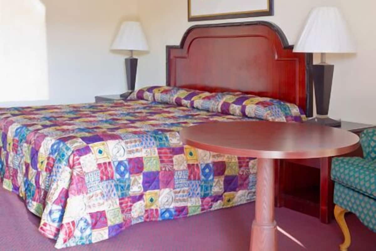 A hotel room with a bed, a round table, two lamps, and a framed picture on the wall.