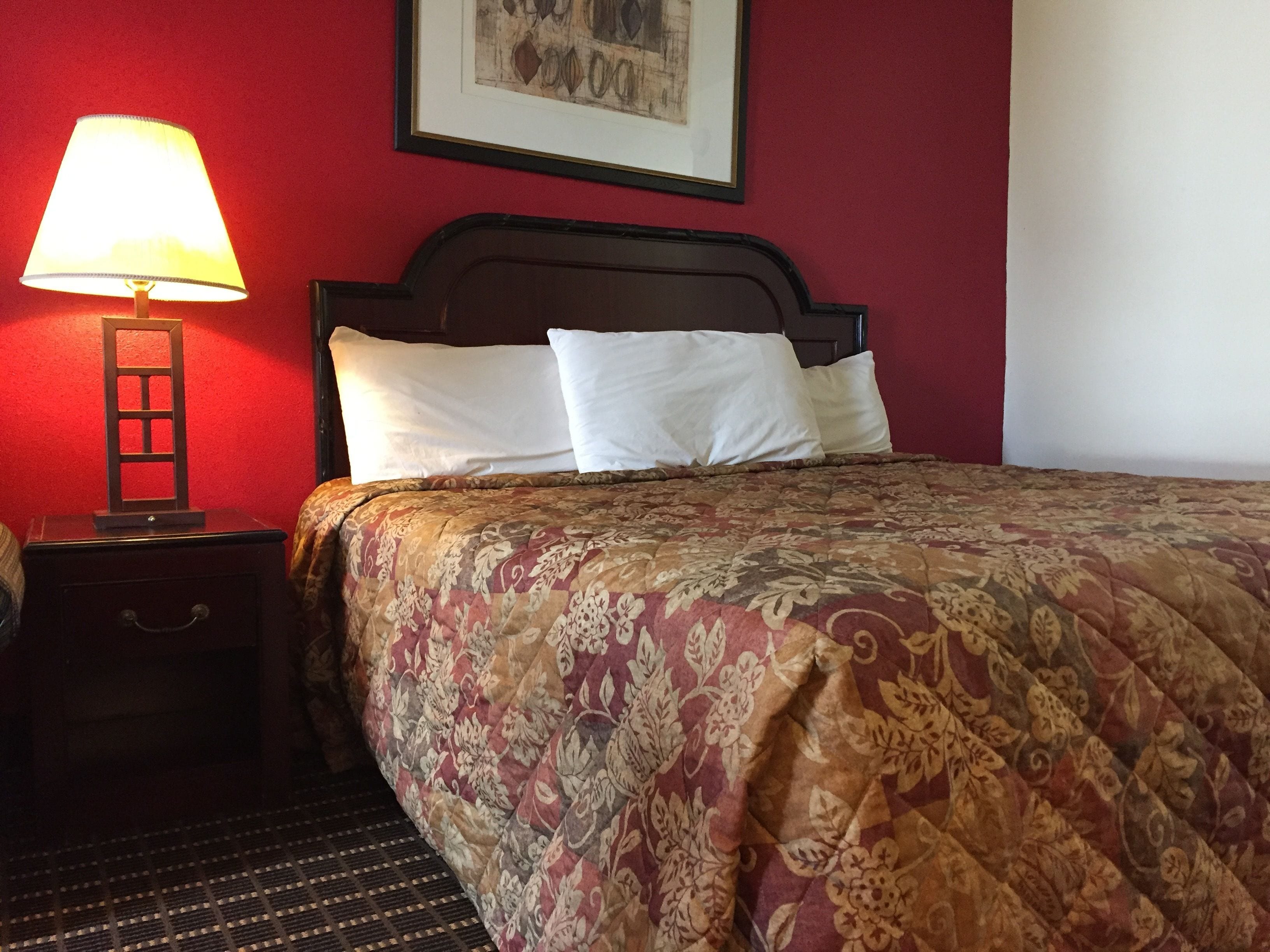 A hotel room with a bed, a nightstand, a lamp, and a framed picture on the wall.