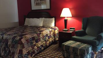 Habitación de hotel con cama, mesita de noche con lámpara, una silla y una alfombra estampada.