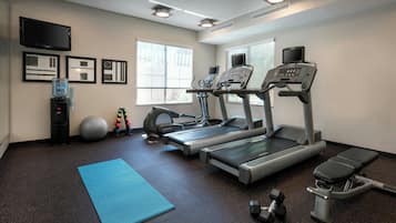 A fitness room with treadmills, a stationary bike, a rowing machine, dumbbells, a yoga mat, and a water dispenser.