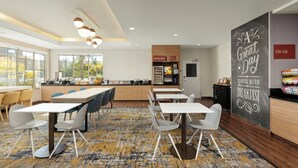 Un comedor moderno con mesas y sillas, una zona de cocina y una pizarra con mensajes motivacionales.