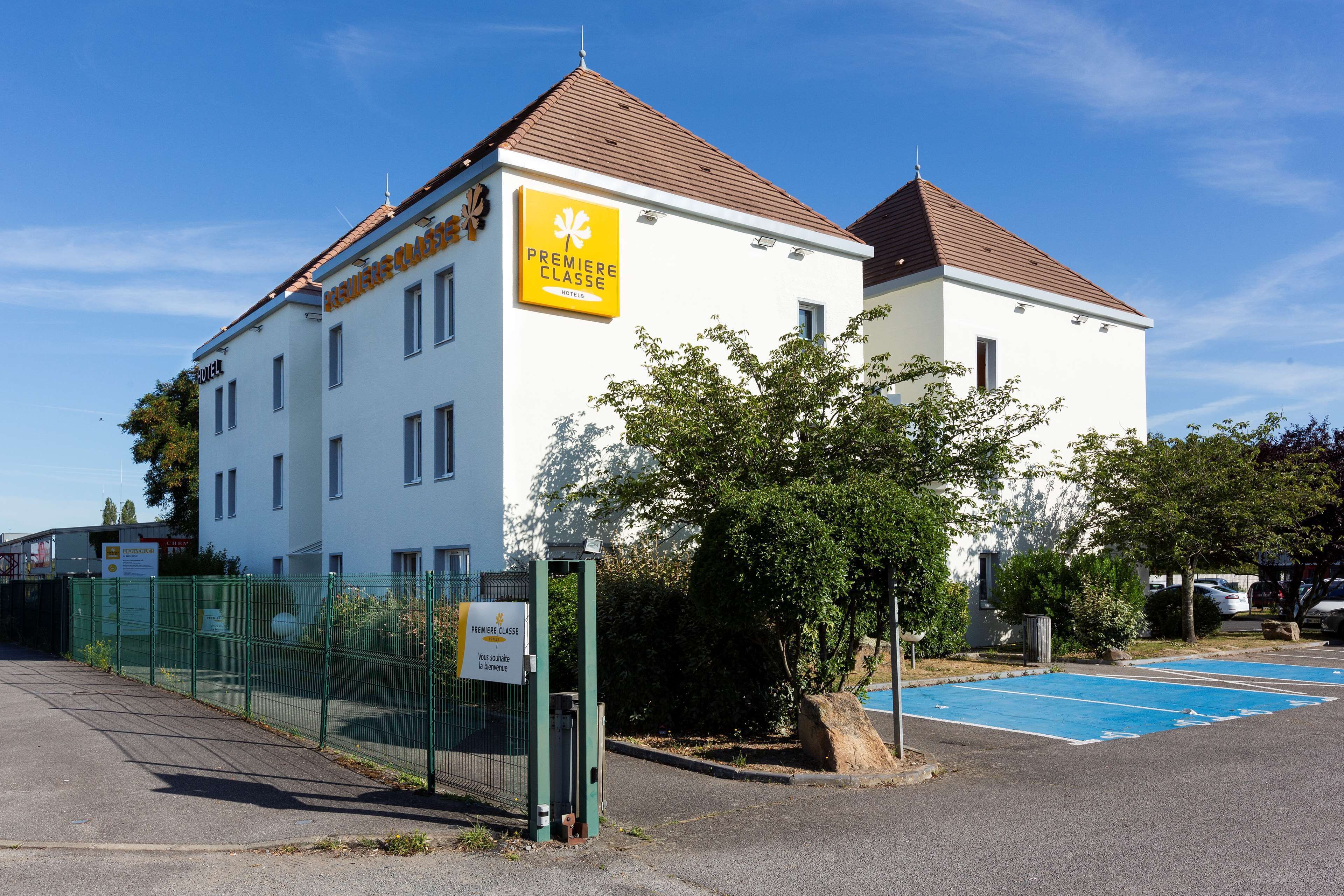 A white building with a sign reading "Premiere Classe" and a fenced parking area.