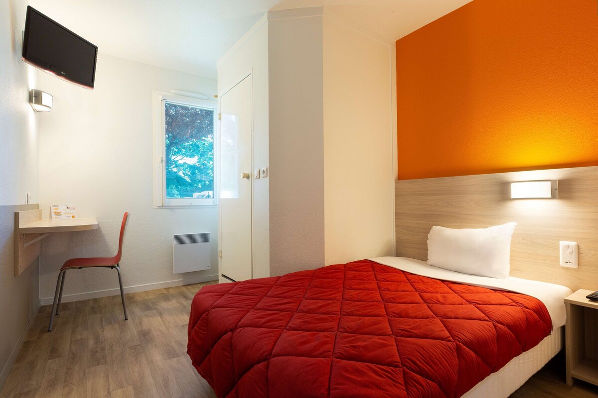 Habitación de hotel con cama, escritorio, silla y ventana con vista a árboles.