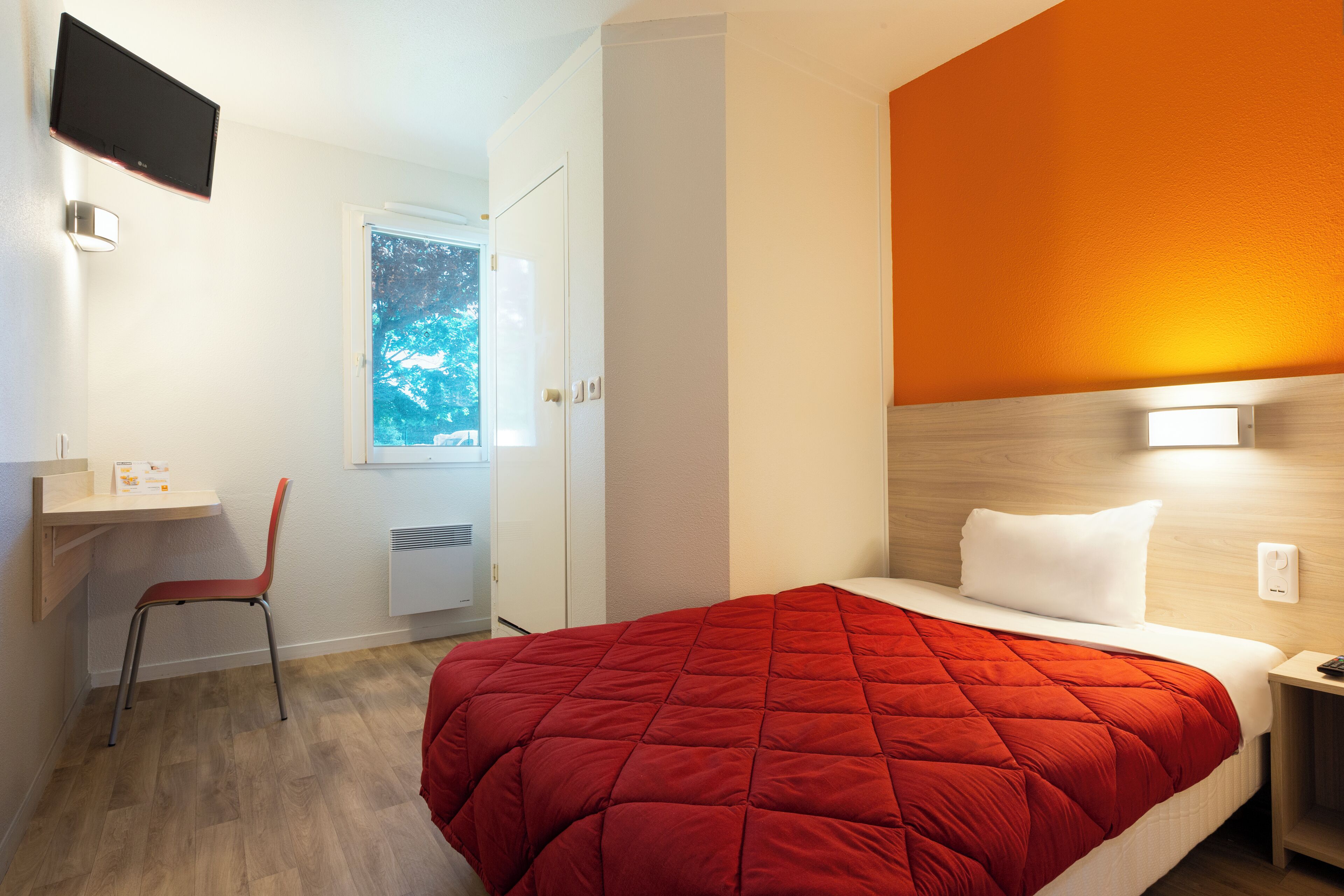 Een hotelkamer met een bed, een bureau, een stoel en een raam met uitzicht op bomen.