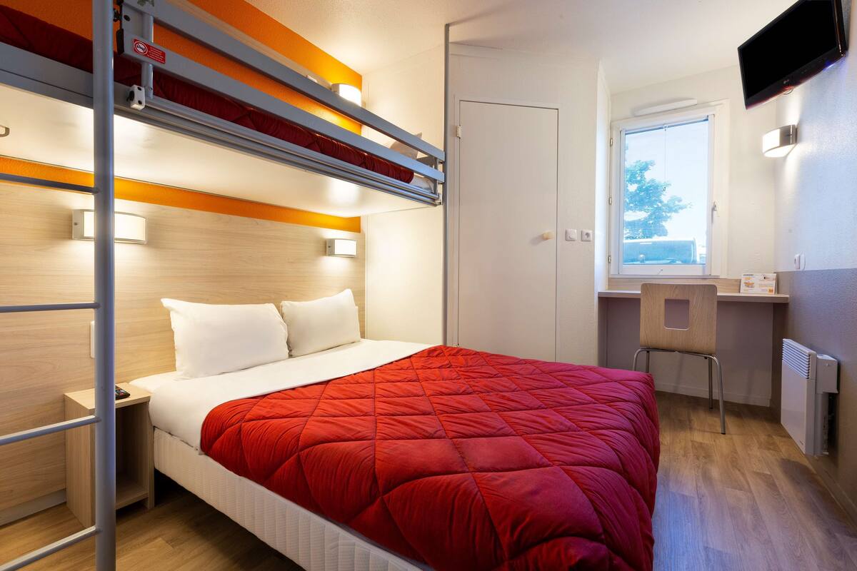 A compact hotel room with a bunk bed, a desk, and a window with a view.