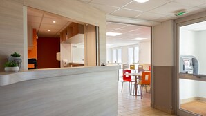 A reception area with a counter, a staircase, and a dining area with chairs and tables. - Première Classe Nantes Ouest - Saint Herblain (Saint-Herblain)