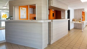 A reception area with a counter, a bulletin board, and a seating area with a table and chairs. - Première Classe Nantes Ouest - Saint Herblain (Saint-Herblain)