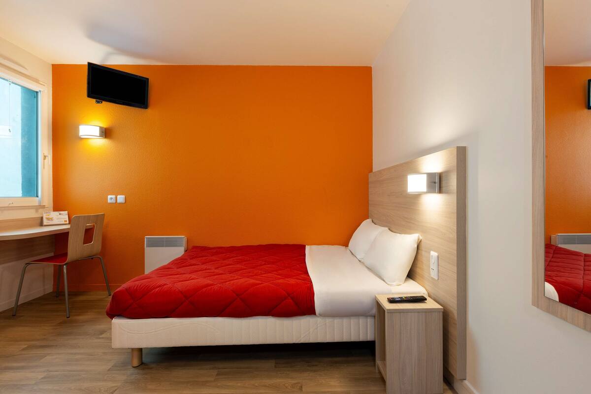 A hotel room with a bed, a desk, a chair, a TV, and a mirror.