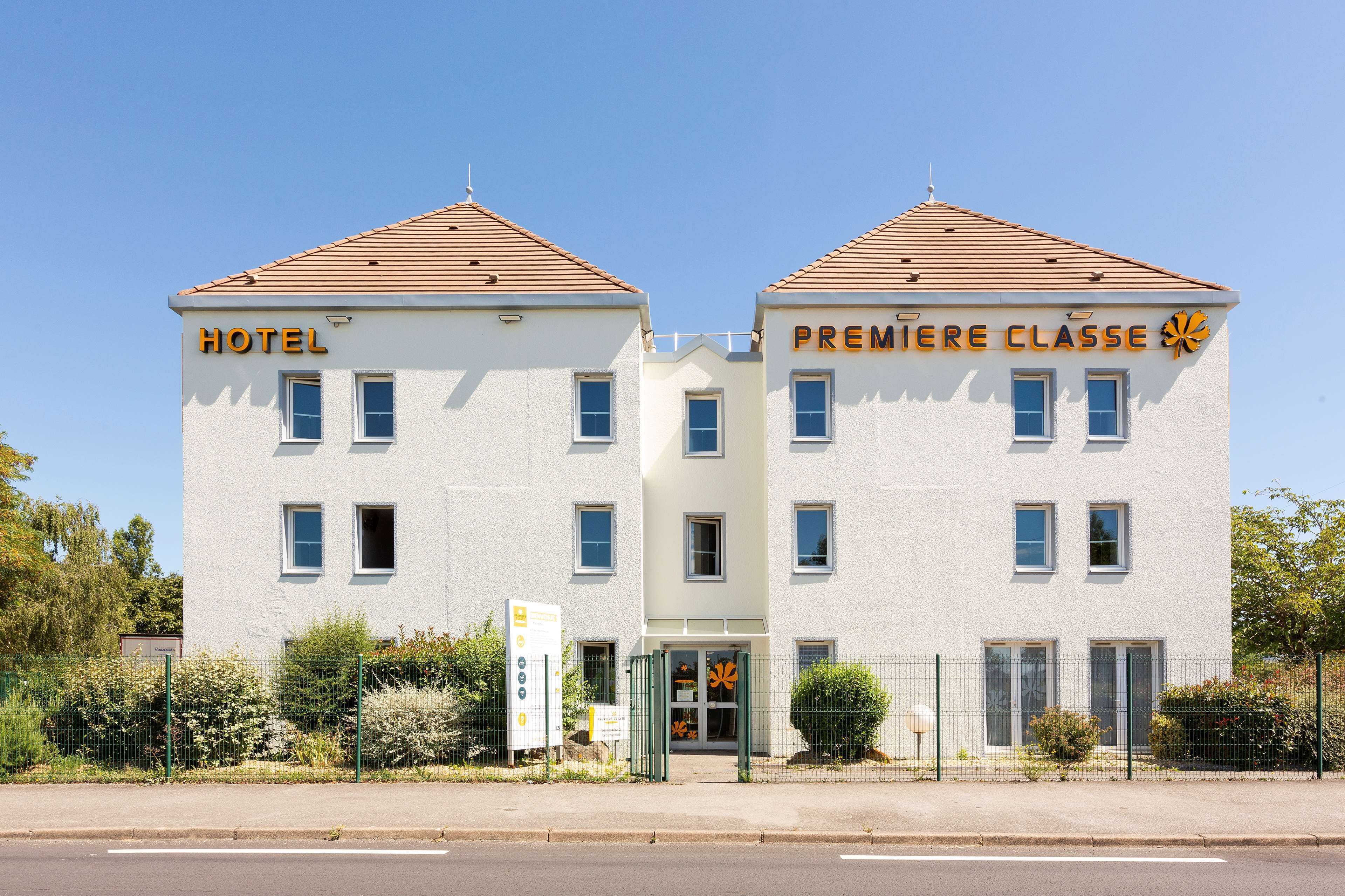 A two-story building with "HOTEL" and "PREMIERE CLASSE" signs, a gated entrance, and a clear sky.