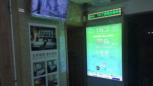 A hotel reception area with a digital display board advertising new rooms and a 3D customer service option. - Venetian Hostel (Kowloon)