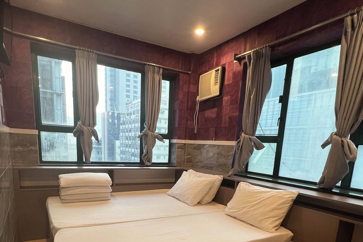 A hotel room with two beds, a window with curtains, a wall-mounted air conditioner, and a pair of shoes on the floor.