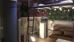 A compact room with a bunk bed, a small desk, a couch, a ladder, a water dispenser, and a wall-mounted phone. - Venetian Hostel (Kowloon)