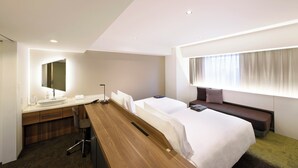 A modern hotel room with a large bed, a desk with a sink, and a seating area by the window.