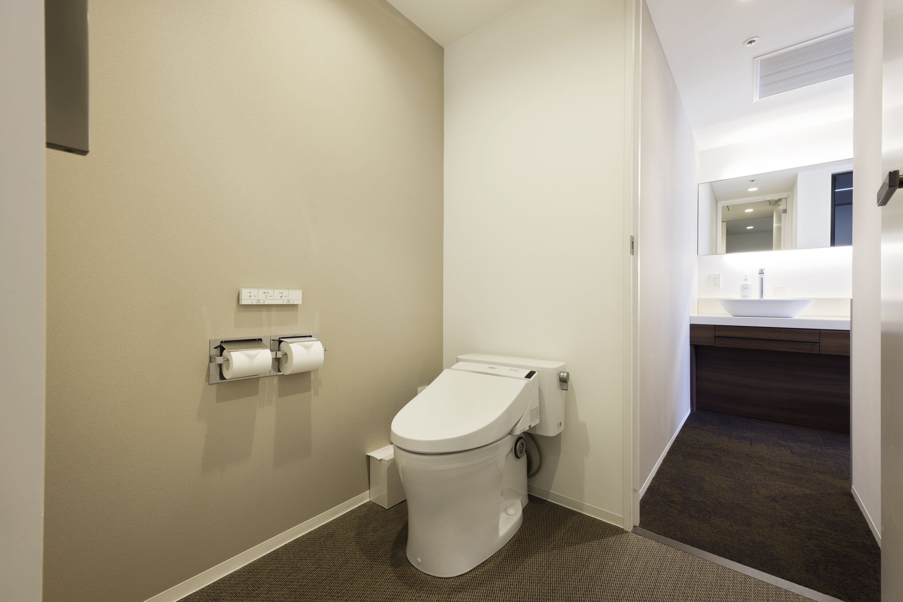 Un baño pequeño y moderno con inodoro blanco, dispensador de toallas y zona de ducha visible.