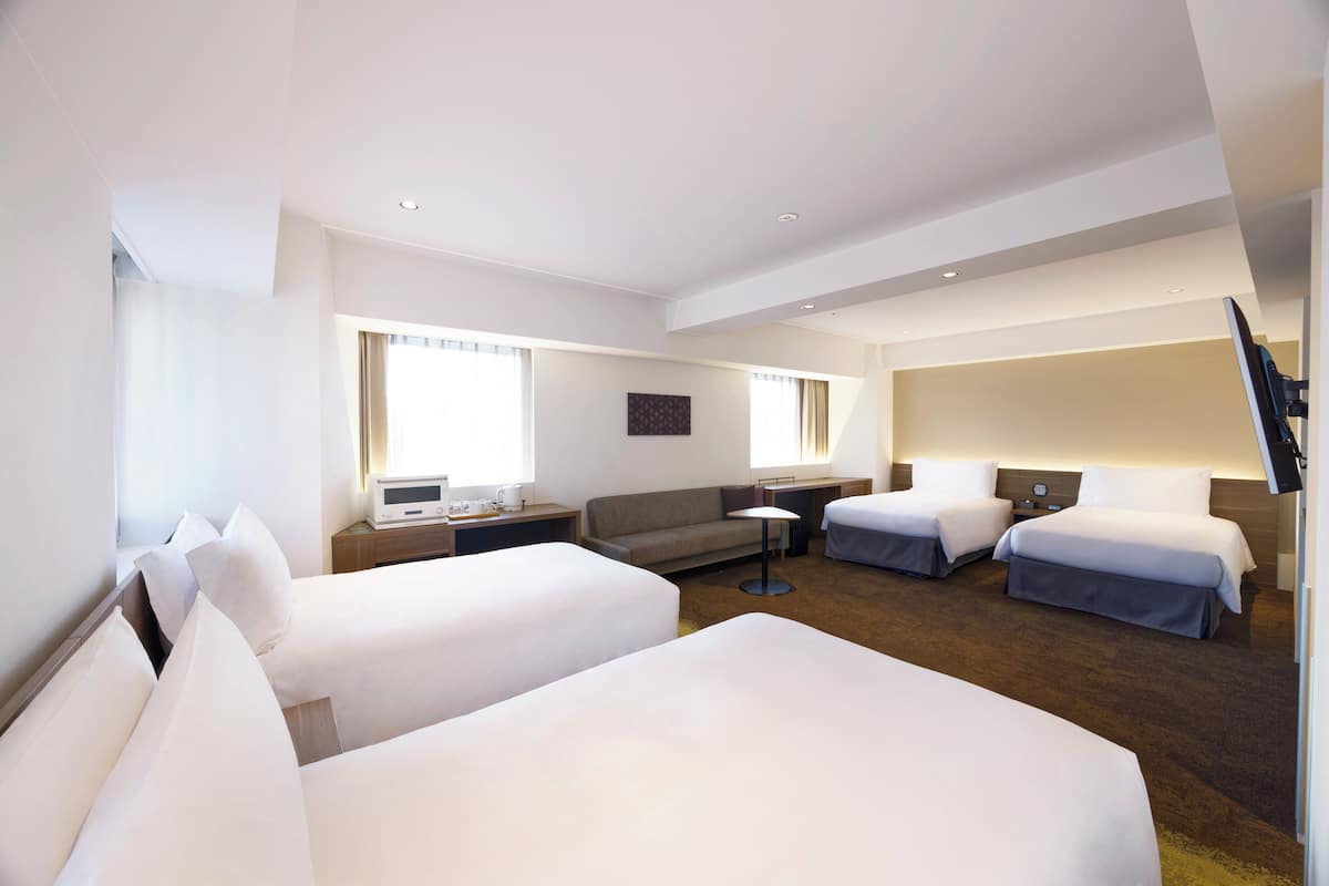 Een hotelkamer met twee eenpersoonsbedden, een slaapbank, een bureau met stoel, een flatscreen-tv en een raam met gordijnen.