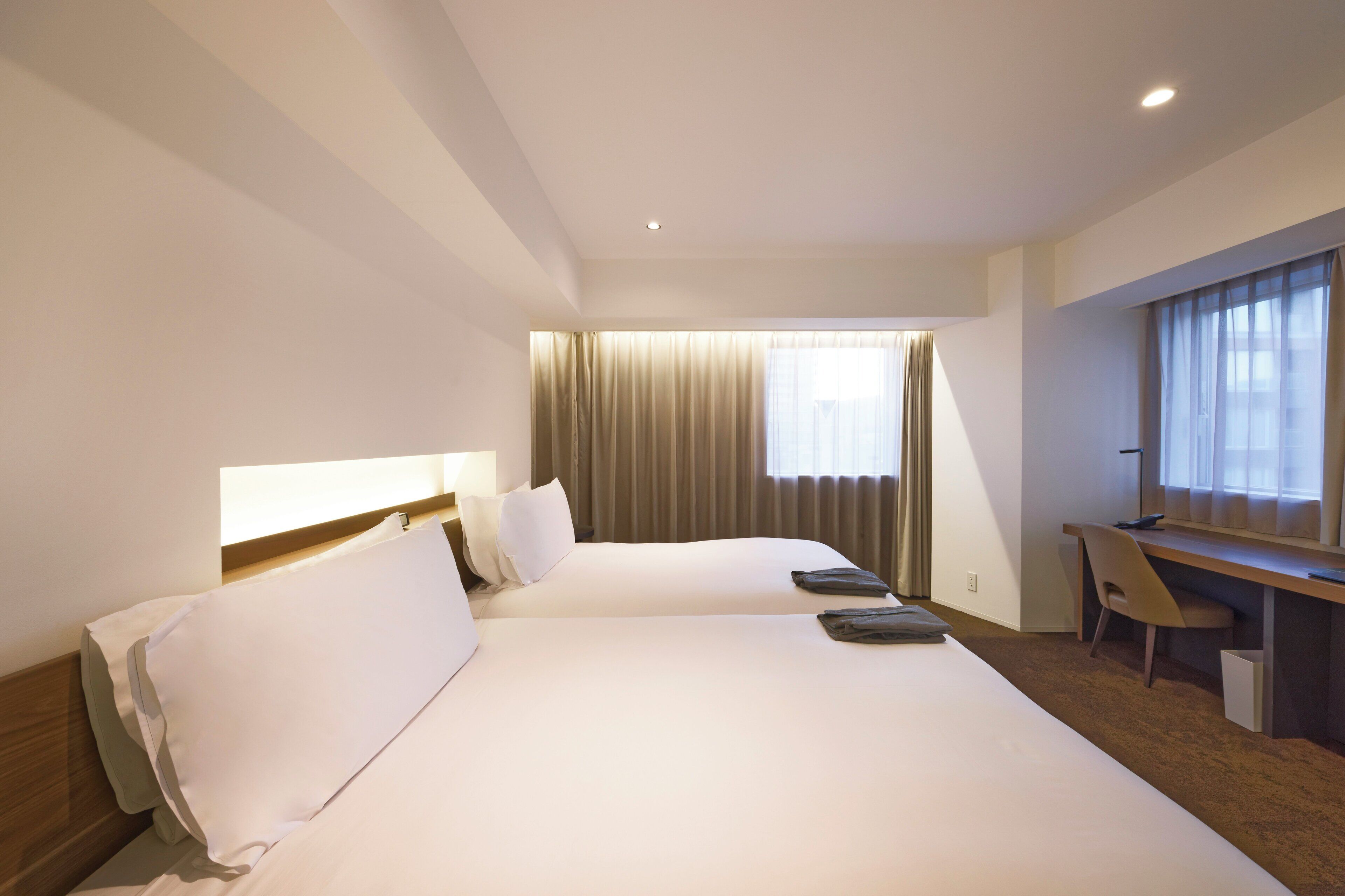 A hotel room with two beds, a desk, and a chair.