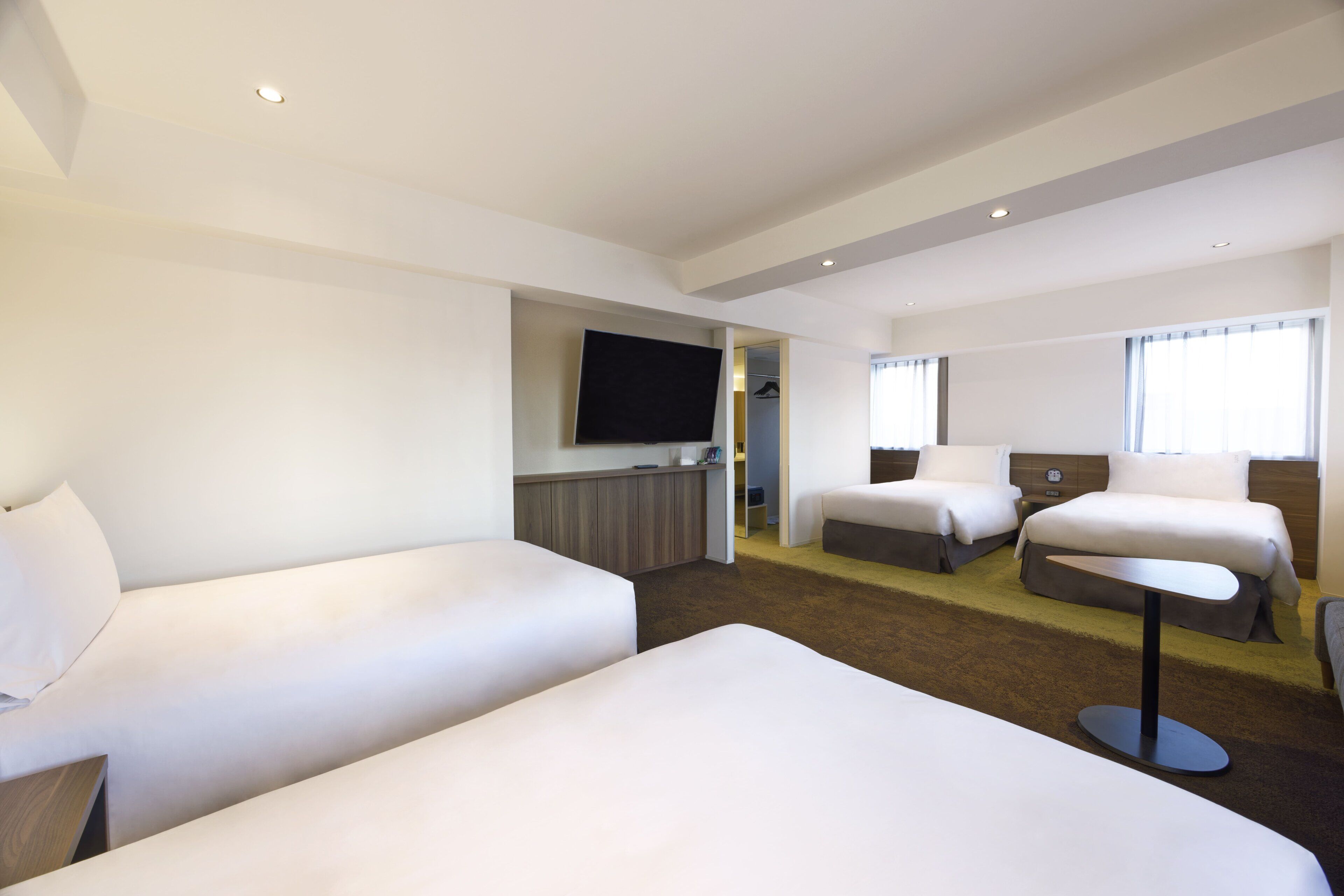 A hotel room with two beds, a flat-screen TV, a small table, and a window with curtains.