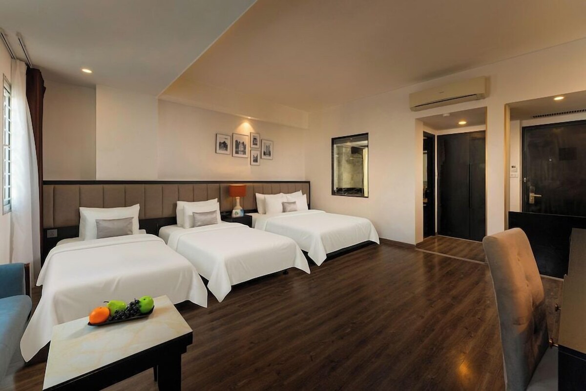 A hotel room with two beds, a desk with fruit, a chair, and a mirror.