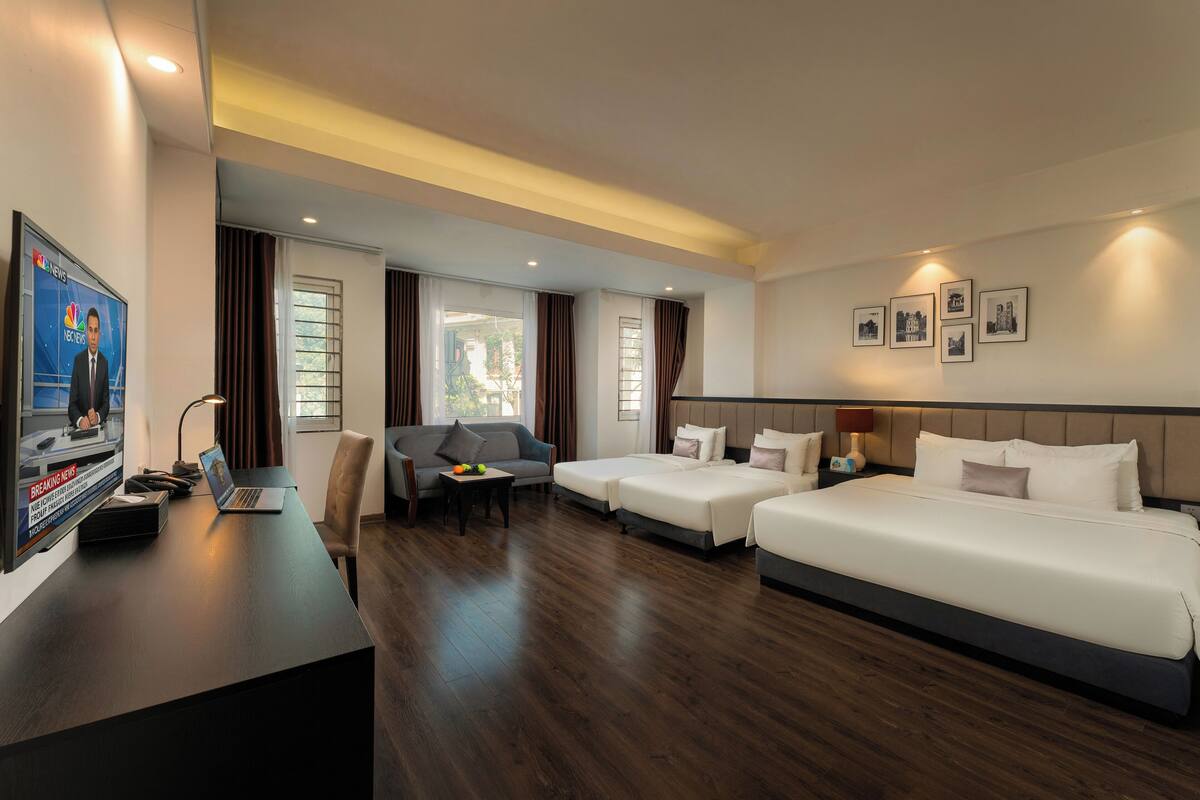 Quarto de hotel com uma cama grande, duas camas menores, uma mesa com um laptop, uma televisão e um sofá.