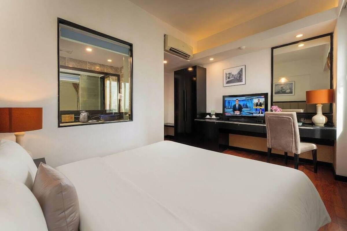 Quarto de hotel com uma cama grande, uma escrivaninha com computador, uma cadeira e uma televisão.