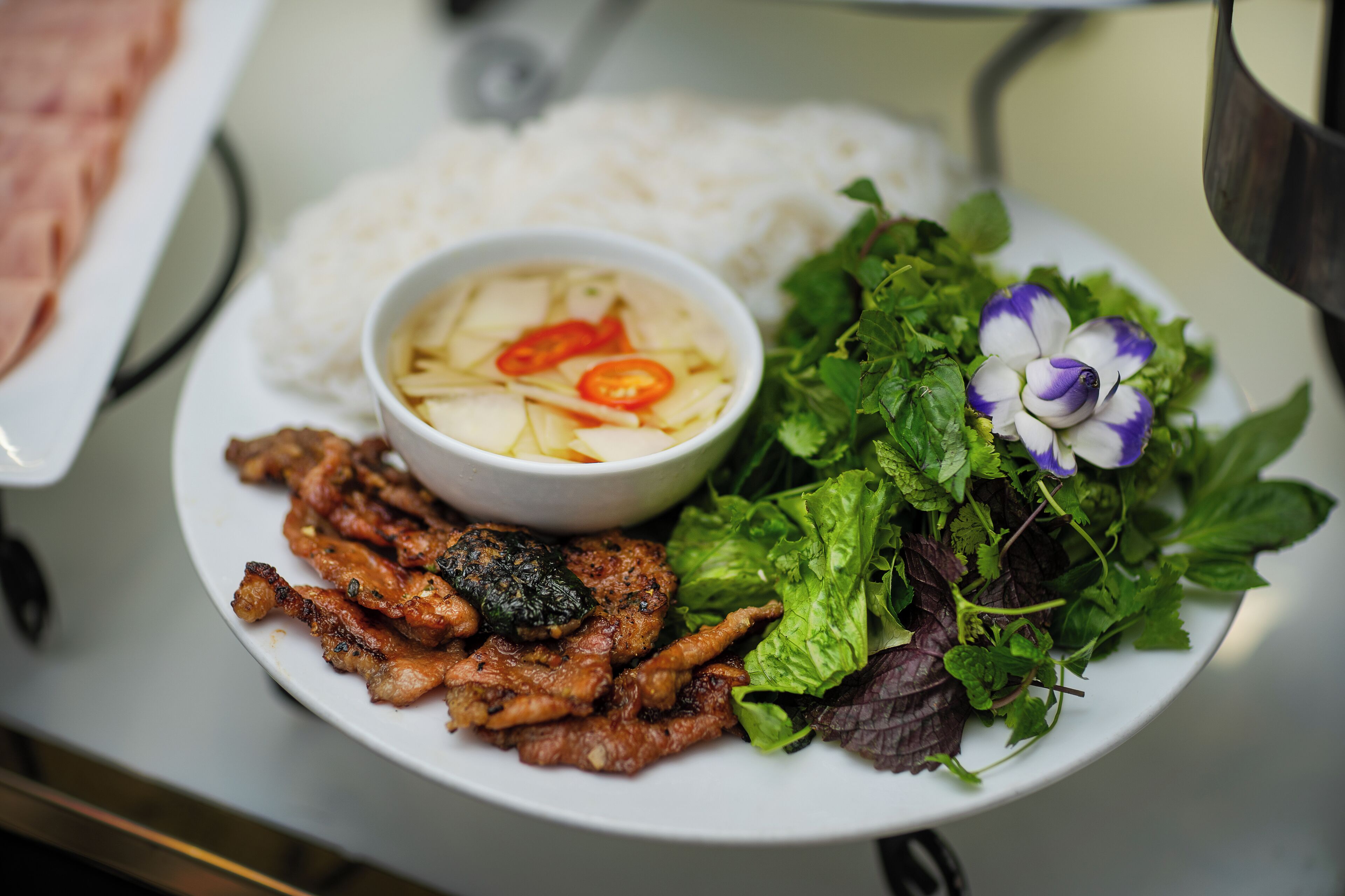 Un plato de arroz, un tazón de sopa, carne a la parrilla y una guarnición de verduras frescas.