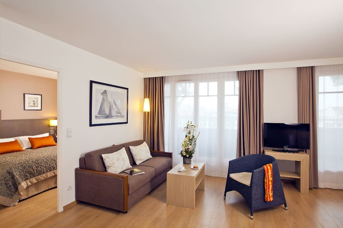 Una habitación de hotel con cama, sofá, televisión, mesa de centro y una silla.