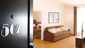 A hotel room with a bed, a brown sofa, a framed picture on the wall, a floor lamp, and a door with the number 502.