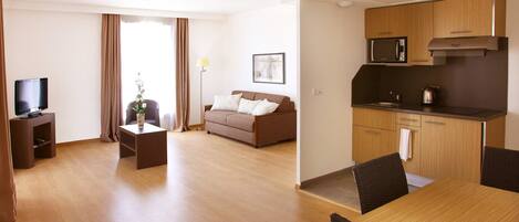 Een moderne hotelkamer met een zithoek, een eettafel, een bank, een televisie en een keuken met een magnetron.