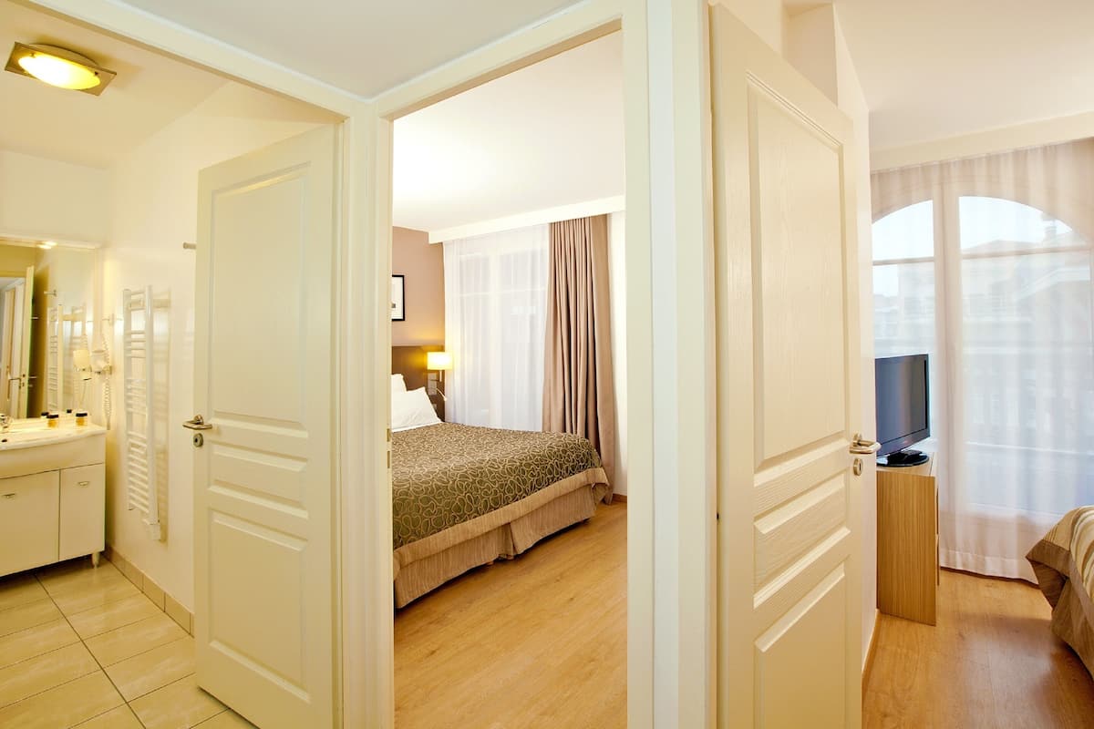 Habitación de hotel con cama, televisor, mesita de noche y baño con espejo y lavamanos.