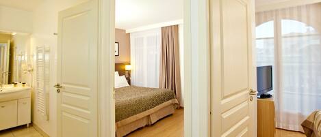 A hotel room with a bed, a TV, a bedside table, and a bathroom with a mirror and sink.