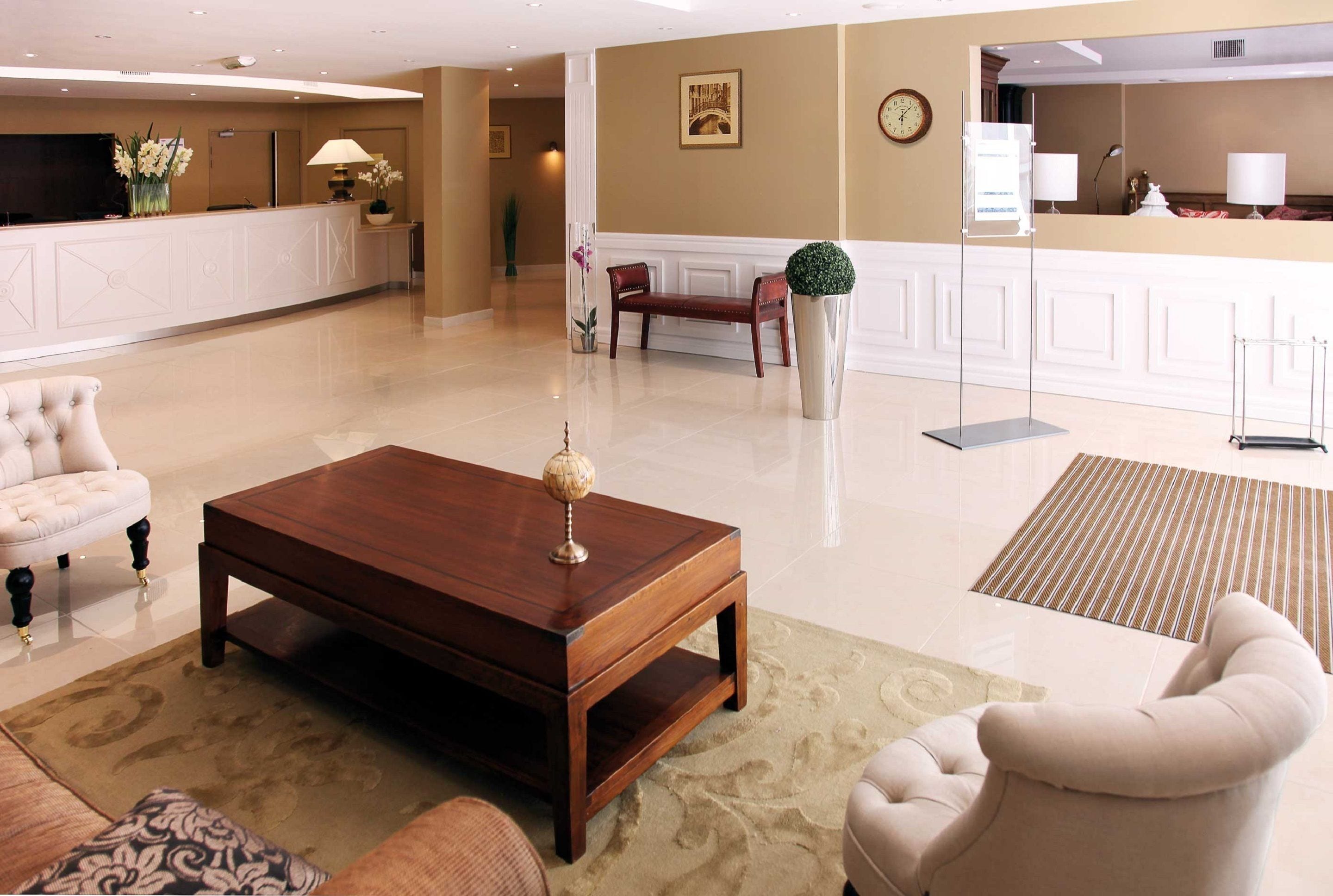 A hotel lobby with a reception desk, a wooden coffee table, and a seating area with a sofa and armchairs.