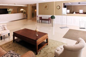 Un hall de hotel con mostrador de recepción, una mesa de centro de madera y una zona de estar con sofá y sillones.