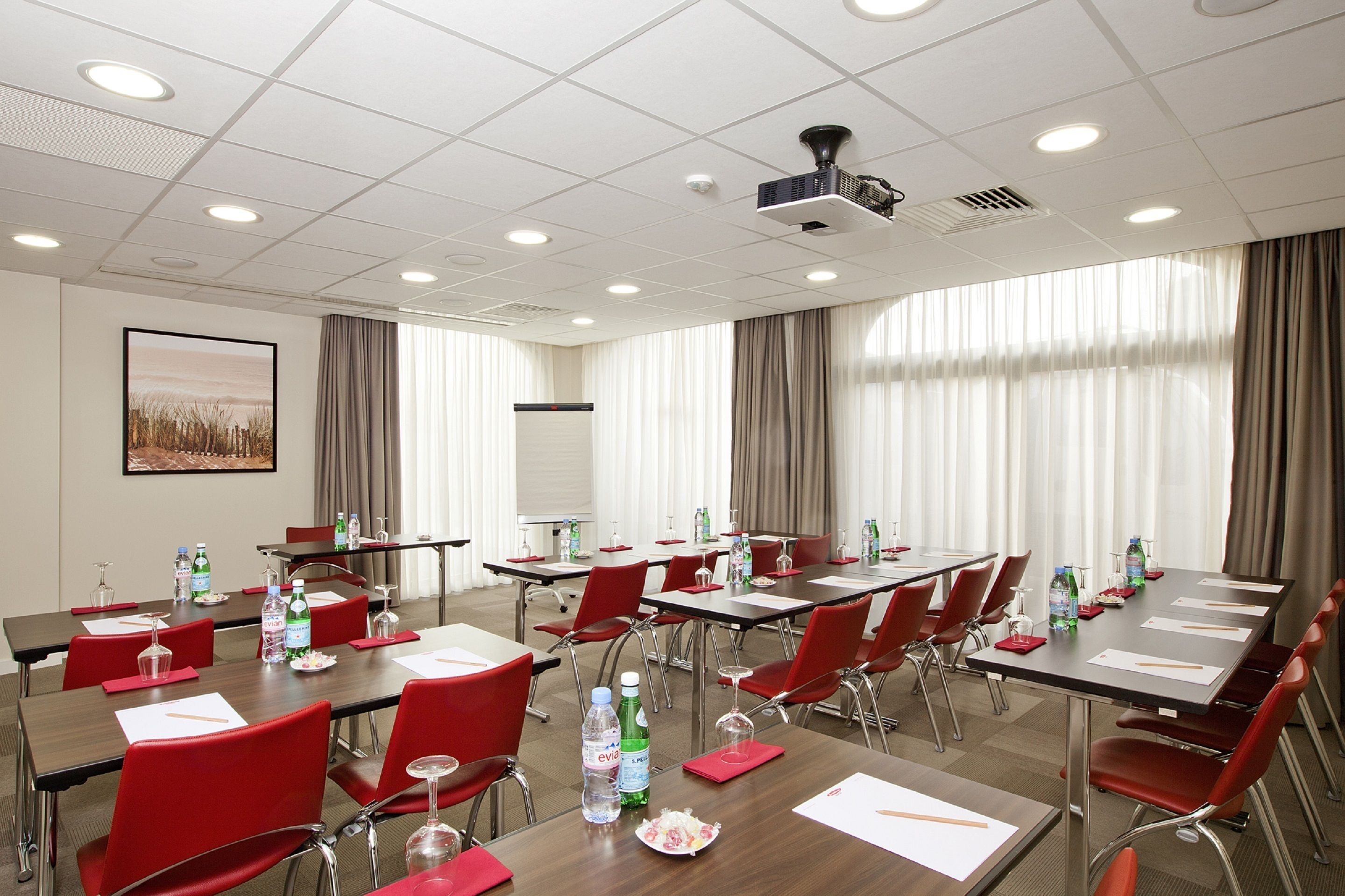 A conference room with multiple tables and red chairs, equipped with water bottles, glasses, and papers.