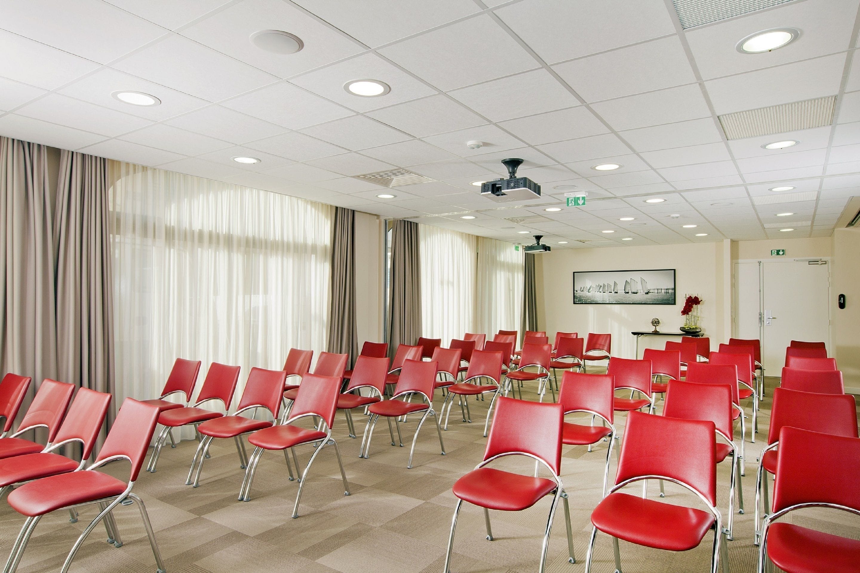 A conference room with rows of red chairs, a projector, and a whiteboard on the wall.
