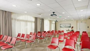 A conference room with rows of red chairs, a projector, and a whiteboard on the wall.