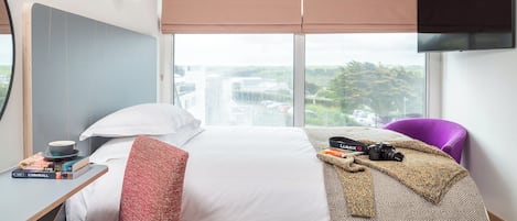 Habitación de hotel con cama, escritorio con libros, cámara y televisor en la pared.