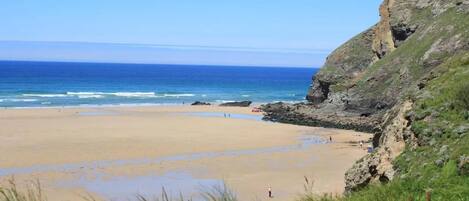 A coastal beach with a rocky cliff and a clear view of the ocean.